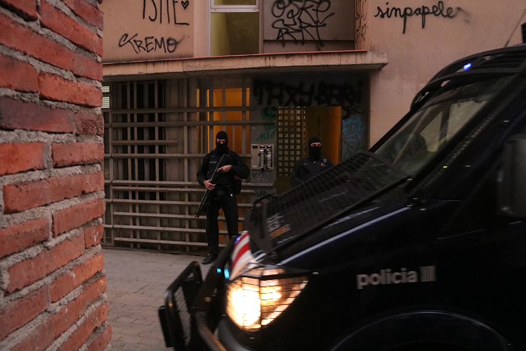 Dos agents i una furgona dels Mossos d'Esquadra custodiant un dels domicilis que s'estan registrant en el marc d'un operatiu policial el 15 de gener del 2019. Foto: Miquel Codolar / ACN.