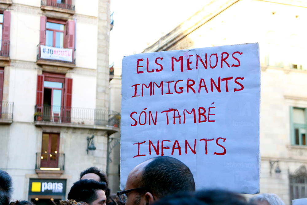 Cartell amb el missatge 'Els menors immigrants són també infants', en la concentració convocada per l'associació Ex-Menas a la plaça de Sant Jaume, el 16 de març del 2019. Foto: Laura Fíguls / ACN